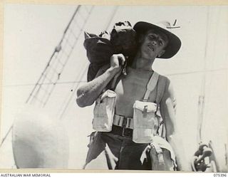 MADANG, NEW GUINEA. 1944-08-19. VX148143 CORPORAL R. RITCHIE, 29/46TH INFANTRY BATTALION, SMILES CHEERFULLY DESPITE HIS HEAVY KITBAG, AS HE MOVES ALONG THE DECK OF HMT "KATOOMBA" BEFORE SHE SAILS ..