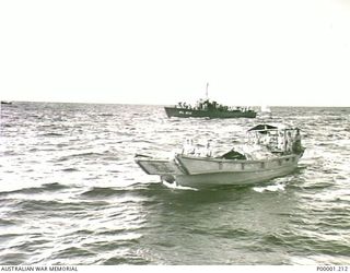 THE SOLOMON ISLANDS, 1945-08-19. JAPANESE BARGE FROM BUIN BAY, BOUGAINVILLE ISLAND, WITH ENVOY OF LIEUTENANT GENERAL MASATANE KANDA, COMMANDER JAPANESE XVII ARMY, ON BOARD APPROACHES HMAS LITHGOW ..