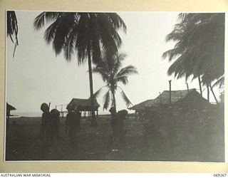 BIAMU, ORO BAY, NEW GUINEA. 1942-11-12. UNITED STATES INFANTRYMEN PASSING THROUGH A NATIVE VILLAGE DURING A HEAVY RAINSTORM