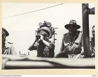 BUT AREA, NEW GUINEA. 1945-02-26. AN AUSTRALIAN ARMY MAJOR AND MILITARY OBSERVER ABOARD THE RAN VESSEL HMAS SWAN SEARCHING OUT THE TARGET AREA DURING A BOMBARDMENT OF THE JAPANESE POSITIONS IN THE ..