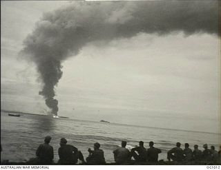 AITAPE, NORTH EAST NEW GUINEA. 1944-04-22. RAAF GROUND PERSONNEL WATCH GREAT CLOUDS OF SMOKE ROLL SKYWARDS FROM A BIG FIRE ON SELEO ISLAND AS THEIR LANDING CRAFT MOVES SHOREWARDS DURING THE EARLY ..