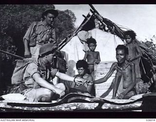 PAPUA, NEW GUINEA, 1942-07. TROOPS OF AN AUSTRALIAN INFANTRY BATTALION ON PATROL IN THE PAPUAN JUNGLE HALT IN A NATIVE VILLAGE AND MAKE FRIENDS WITH THE INHABITANTS