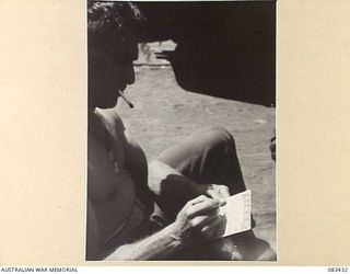 AT SEA, NEW GUINEA AREA. 1944-11-12. PRIVATE J. BISSETT, 2/11 INFANTRY BATTALION, CONCENTRATING ON A GAME OF "BINGO" ON THE FORWARD WELL DECK ABOARD USS MEXICO