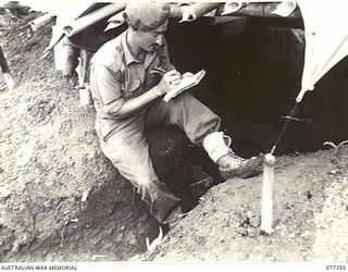 TOROKINA AREA, BOUGAINVILLE ISLAND. 1944-11-30. Q16828 PRIVATE F.W.A. TIMM, C COMPANY, 9TH INFANTRY BATTALION, WRITING A LETTER HOME, SEATED IN FRONT OF HIS DUGOUT ON LITTLE GEORGE HILL, A FEATURE ..