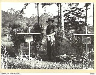 RAK VILLAGE, NEW BRITAIN. 1945-01-17. NX51929 SERGEANT A.N. TAYLOR (1) AND NGN314 LANCE CORPORAL SAKAP, "B" COMPANY, 1ST NEW GUINEA INFANTRY BATTALION STANDING BY THE GRAVES OF TWO MEMBERS OF THE ..