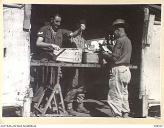 CAPE WOM, WEWAK, NEW GUINEA, 1945-07-31. PRIVATE C.B. MORRIS (2) RECEIVING CANTEEN GOODS FROM SERGEANT G.A. LUSH (1), BOTH MEMBERS OF CANTEEN BULK STORES AND ISSUING POINT OPERATED BY AUSTRALIAN ..