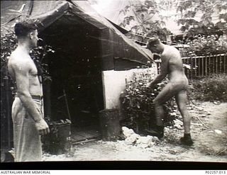 Madang, New Guinea, 1945-08-03. Stark naked except for a pair of boots, 82586 Flying Officer Allen Robert Griffiths (right), Administrative and Special Duties (A&SD) Intelligence, Headquarters, ..