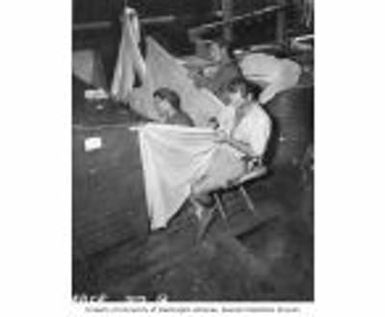 Commercial fishermen aboard LSM 382 sewing bait seine on fish nets, Rongerik Island, summer 1947
