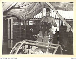 LAE, NEW GUINEA. 1944-12-12. WARRANT OFFICER II W.F. LOY, ARMY CANTEENS SERVICE, SECOND IN CHARGE OF A SOFT DRINK FACTORY IN THE LAE BASE SUB-AREA REMOVES ONE OF THE WIRE GAUZE FILTERS FROM AN ..