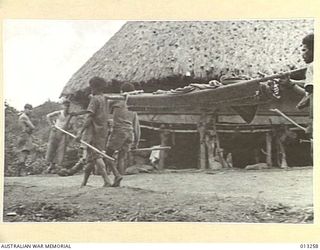 OWEN STANLEY RANGES, NEW GUINEA. 1942-09-05. WOUNDED AUSTRALIANS BEING CARRIED ON STRETCHERS OUT OF FORWARD BATTLE AREAS INTO A VILLAGE BY NATIVE BEARERS OR PORTERS (KNOWN AS FUZZY WUZZY ANGELS)