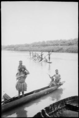 Two women and two children in a canoe with eight men standing in a second canoe, Ramu River, New Guinea, 1935 / Sarah Chinnery