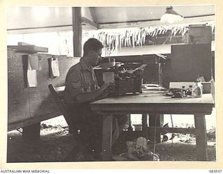 LAE, NEW GUINEA. 1944-12-12. SERGEANT V. COLLINS, 2 FIELD TEAM, MILITARY HISTORY SECTION, ATTACHED HEADQUARTERS FIRST ARMY, LAE BASE SUB-AREA, WORKING AT HIS OFFICE DESK