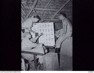 PORT MORESBY, PAPUA, 1942-07-11. THREE AMERICAN FIGHTER-PILOTS STUDYING THE IDENTIFICATION CHART OF JAPANESE AIRCRAFT. THEY ARE FLYING AIRA-COBRA FIGHTER-PLANES IN THE NEW GUINEA WAR ZONE