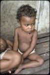 Young child wearing shell necklace, sits next to mother and young infant