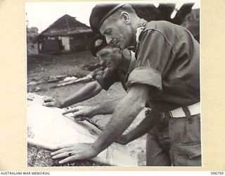 KARAWOP, NEW GUINEA, 1945-09-18. LT-COL E.C. HENNESSY (1) AND CAPT N.V. WOODHOUSE (2), MEMBERS OF 2/6 CAVALRY COMMANDO REGIMENT, EDUCATION SECTION, DISCUSS PROPOSED CAMP SITE AND TAKE NOTES FROM ..