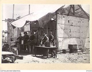 ALEXISHAFEN, NEW GUINEA. 1944-05. THE KITCHEN STAFF, 2/15TH FIELD AMBULANCE, PREPARING DINNER NEAR ONE OF THE WRECKED BUILDINGS AT THE OLD CATHOLIC MISSION. MANY OF THE MISSION'S BUILDINGS HAVE ..