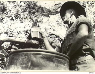 BOUGAINVILLE. 1944-11-24. SX33273 LANCE-CORPORAL D.K. STUART, FIELD SECURITY SECTION ATTACHED TO 9TH INFANTRY BATTALION FILLING HIS WATER BOTTLE FROM A BAMBOO PIPE WHICH CARRIES FRESH WATER FROM A ..