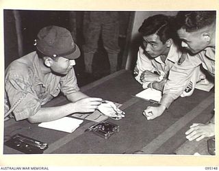 TOKO, BOUGAINVILLE, 1945-08-18. MAJOR OTSU (1), MEMBER OF A SURRENDER ENVOY FROM LIEUTENANT-GENERAL M. KANDA, COMMANDER IMPERIAL JAPANESE 17 ARMY GROUP, HOLDS OUT HIS WATCH WHEN SYNCHRONISING TIMES ..