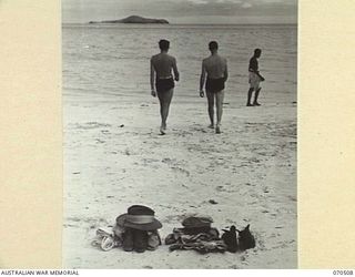 PORT MORESBY, PAPUA, 1944-02. AN AMERICAN OFFICER AND AN AUSTRALIAN SOLDIER HEAD FOR THE WATER AFTER LEAVING THEIR CLOTHES NEATLY STACKED ON THE BEACH