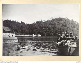 NANTAMBU, NEW BRITAIN, 1945-08-22. A LAUNCH LOADED WITH 37/52ND INFANTRY BATTALION TROOPS AWAITING MOVEMENT TO A ROYAL NEW ZEALAND AIR FORCE CATALINA AIRCRAFT; ANOTHER CATALINA IS TAKING OFF IN THE ..