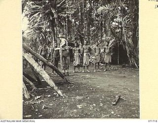 SINGORKAI - WEBER POINT AREA, NEW GUINEA, 1944-03-21. CARRIERS WITH MEMBERS OF THE PAPUAN INFANTRY BATTALION RECEIVING PAYMENT IN STICKS OF TRADE TOBACCO AT GALI NO. 2 VILLAGE. THE CARRIERS ARE ..