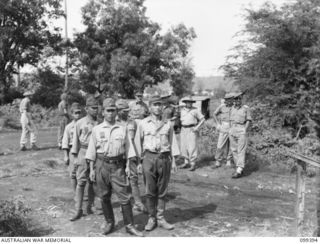 RABAUL, NEW BRITAIN, 1945-12-11. FIVE JAPANESE WAR CRIMINALS LINED UP OUTSIDE THE WAR CRIMES COURT, HEADQUARTERS 11 DIVISION, WAITING COMMENCEMENT OF THEIR TRIAL. AUSTRALIAN STAFF OFFICERS ARE IN ..
