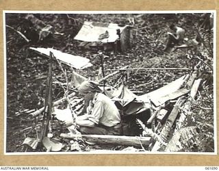 WAREO, NEW GUINEA. 1943-12-09. VX25125 LIEUTENANT R. S. BARRAND OF A COMPANY, 2/23RD AUSTRALIAN INFANTRY BATTALION SITTING IN HIS TRENCH READING A LETTER FROM HOME