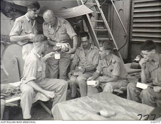 AT SEA IN THE ADMIRALTY ISLANDS AREA. 1944-03-18. THERE ARE NO OFFICERS' MESS COMFORTS ON CROWDED LANDING CRAFT. RAAF OFFICERS EATING THEIR LUNCH ARE: FLYING OFFICER (FO) L. B. SODEN, DORRIGO, NSW; ..