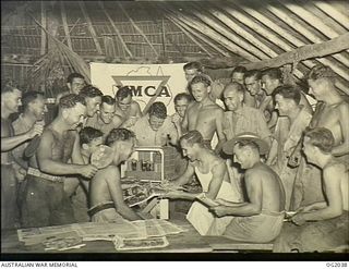 Members of an AIF Bakery Unit "somewhere in New Guinea" at a YMCA hut with RAAF personnel listiening to racing descriptions re-broadcast from the ABC short-wave service during stand-down afternoon. ..