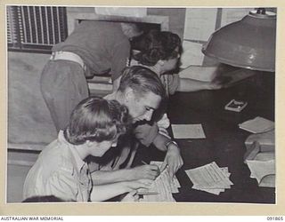 LAE, NEW GUINEA, 1945-05-16. SIGNALMAN V. CORNEY (1), AND SIGNALWOMAN L.A. WILLIAMS (3), SIGNAL CLERKS AT HEADQUARTERS FIRST ARMY ARE BEING SHOWN THEIR NEW DUTIES BY SIGNALMAN I.C. PLOENGERS, (2). ..