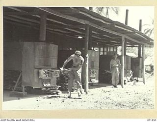 LAE, NEW GUINEA. 1944-03-30. QX59066 PRIVATE D. O. MARRABLE (LEFT), STOKING ONE OF THE FOUR FIRE BOXES IN THE STEAMPIPE OVENS AT THE 8TH FIELD BAKING PLATOON. STANDING AT THE BACKGROUND IS QX47381 ..