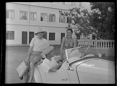 Suzanne and unidentified men sitting in a convertible MG car, Tahiti