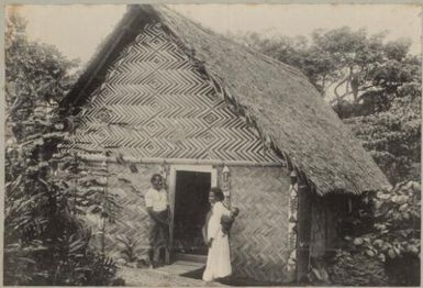 Man and a woman carrying a child standing at the doorway of a traditional house, Tonga? approximately 1895