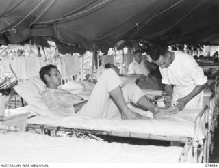 LAE. NEW GUINEA. 1944-07-14. VX10486 PRIVATE H. ANDREWS, MEDICAL ORDERLY (1) PAINTING THE FOOT OF NX120727 SERGEANT R.C. FALKARD WITH GENTIAN VIOLET IN ONE OF THE WARDS OF THE 2/7TH AUSTRALIAN ..