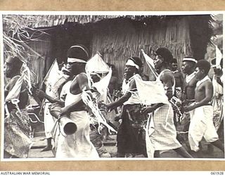 KILA KILA, PAPUA, NEW GUINEA. 1943-12-25. KEREMA BOYS EXECUTING A DANCE AT THE AUSTRALIAN AND NEW GUINEA ADMINISTRATION UNIT NATIVE LABOUR CAMP. THE DANCERS WEAR LONG TRAILS OF GRASS AND FLOWERS, ..