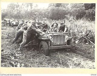 BOUGAINVILLE ISLAND. 1945-03-01. A BOGGED JEEP AND TRAILER OF THE 7TH INFANTRY BATTALION BEING MANHANDLED OUT OF THE BOG IN ORDER TO GET IT THROUGH IN TIME TO CONNECT UP WITH THE JEEP TRAIN FOR ..