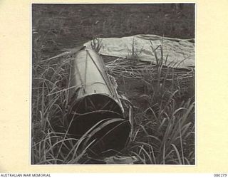 NADZAB, NEW GUINEA. 1944-10-21. A STORPEDO CONTAINING STORES AND PROVISIONS DROPPED BY PARACHUTE TO PERSONNEL OF HEADQUARTERS NEW GUINEA FORCE. THE BROKEN PERCUSSION NOSE, (FOREGROUND), IS DESIGNED ..