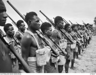 BOUGAINVILLE ISLAND. 1945-01-25. TROOPS OF "A" COMPANY, 1ST NEW GUINEA INFANTRY BATTALION WITH RIFLES AT THE SLOPE DURING THE UNIT MORNING PARADE OUTSIDE THEIR COMPANY HEADQUARTERS SOUTH OF THE ..