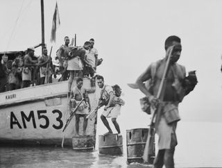 SINGORKAI, NEW GUINEA. 1944-03-19. NATIVE SOLDIERS OF A PLATOON, C COMPANY, PAPUAN INFANTRY BATTALION UNLOADING FROM THE AM53 KAURI WITH A DETACHMENT OF SIGNALS AND CIPHER PERSONNEL, TOGETHER WITH ..