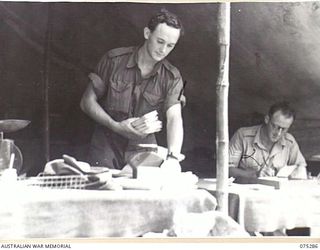 MADANG, NEW GUINEA. 1944-08-15. NX120024 CORPORAL A. WALKER, POSTAL ORDERLY (1) AND NX164899 SERGEANT P.A. TRY, PAY SERGEANT (2) OF THE 165TH GENERAL TRANSPORT COMPANY WORKING IN THEIR TENT OFFICE