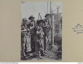 WEWAK POINT, NEW GUINEA, 1945-05-12. 2/4 INFANTRY BATTALION MORTAR MEN PASS SIGNS DENOTING THE BATTLE AREA. THE SIGNS, REMINDERS OF SYDNEY, WERE ON THE ORDERS FOR BATTLE AND WERE ERECTED ..