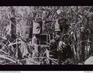 BUNA, NEW GUINEA. 1943. A STILL OPERATED BY GUNNER JACK CASTLEDINE (LEFT) AND GNR JIM BOURKE (RIGHT) OF 8 BATTERY, 2/3RD LIGHT ANTI AIRCRAFT REGIMENT, HIDDEN IN THE JUNGLE NEAR ONE OF THE BATTERY'S ..