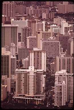 MASSED HIGHRISES OF WAIKIKI DISTRICT, FAVORITE OF TOURISTS SEEN FROM TOP OF DIAMOND HEAD, THE FAMOUS EXTINCT VOLCANO. THE WAIKIKI IMPROVEMENT ASSOCIATION HAS FORMED AN ARCHITECTURAL DESIGN REVIEW BOARD TO OVERSEE SUCH BUILDING, BUT IT IS PROBABLY TOO LATE. IN 1963 THERE WERE 9,203 HOTEL ROOMS IN ALL OF OAHU ISLAND. TODAY THERE ARE SOME 26,000 ROOMS, MOST OF THEM HERE IN WAIKIKI