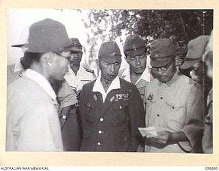 SAMANSO ISLAND, SOLOMON ISLANDS. 1945-11-13. A GROUP OF JAPANESE OFFICERS, AMONG THEM LIEUTENANT GENERAL M. KANDA, COMMANDER 17 JAPANESE ARMY (CENTRE), LOOKING AT A NEWSPAPER CUTTING REPORTING WAR ..