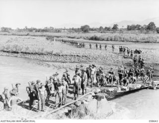 GUSAP RIVER, NEW GUINEA, 1943-10-04. TROOPS OF THE 2/6TH AUSTRALIAN FIELD COMPANY, ROYAL AUSTRALIAN ENGINEERS WORKING TO COMPLETE A BRIDGE, AS TROOPS OF THE 2/14TH AUSTRALIAN INFANTRY BATTALION ..