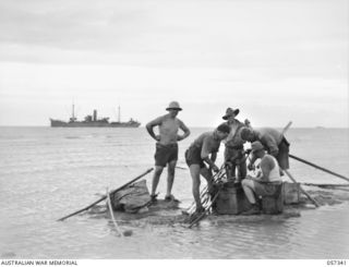 BOERA POINT, NEW GUINEA. 1943-10-01. TROOPS OF THE SIGNALS SECTION, NEW GUINEA FORCE SPLICING SHORE END OF SUBMARINE CABLE TO BEACH CABLE. THE SS MERNOO MARINE CABLE LAYING SHIP CAN BE SEEN IN THE ..