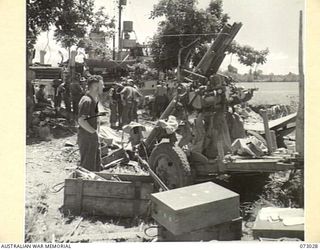 ALEXISHAFEN, NEW GUINEA. 1944-04-27. THE AREA NEAR THE WATERFRONT SHOWING CASES OF ABANDONED JAPANESE EQUIPMENT AND THE RESULTS OF ALLIED BOMBING. A MEMBER OF THE RAN (1), AT THE FOREGROUND ..