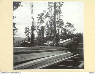 BUSU FOREST, LAE AREA, NEW GUINEA. 1944-07-26. NATIVE LABOUR SUPPLIED BY THE AUSTRALIAN NEW GUINEA ADMINISTRATIVE UNIT LOAD SCANTLINGS FROM YARD STACKS AT THE 2/3RD FORESTRY COMPANY, ROYAL ..