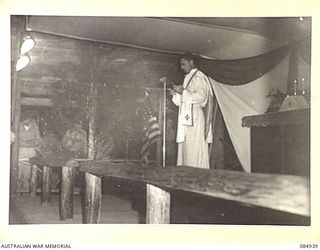 TOROKINA AREA, BOUGAINVILLE, SOLOMON ISLANDS. 1944-12-24. MAJOR P FLAHERTY, CHAPLAIN, 14 CORPS, UNITED STATES ARMY, CONDUCTING A COMBINED AUSTRALIAN AND AMERICAN MIDNIGHT MASS ON CHRISTMAS EVE