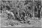 Smiling group of boys and men gather plant debris by government rest house in Tsembaga